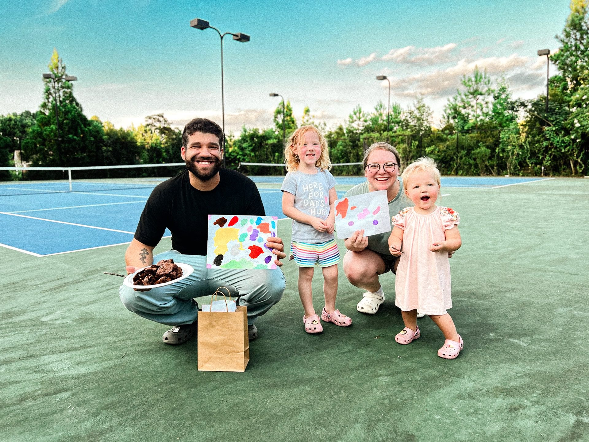 photo of Jacob, Ellie, Allyssa, and Emmie on the tennis court at our apartment celebrating Jacob's birthday with brownies and homemade cards